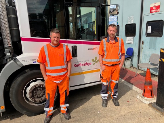 Two men standing in high visibility clothing next to a bin lorry