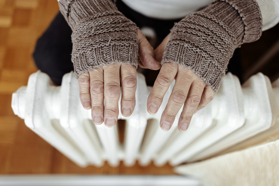 Old men's hands in knitted gloves on heating radiator at home during the day