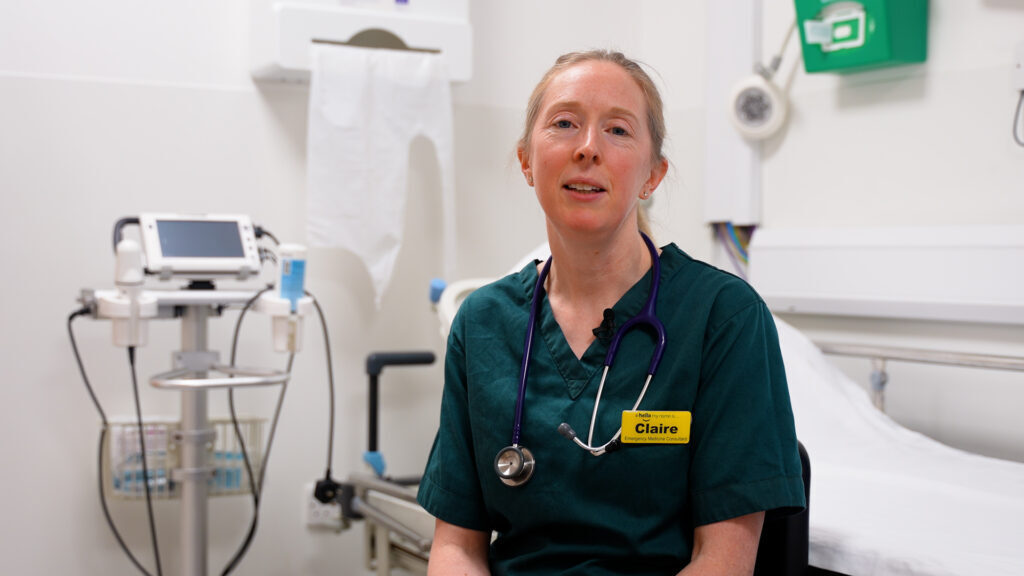  A woman in a hospital gown sits in a chair, appearing contemplative and calm in a medical setting.