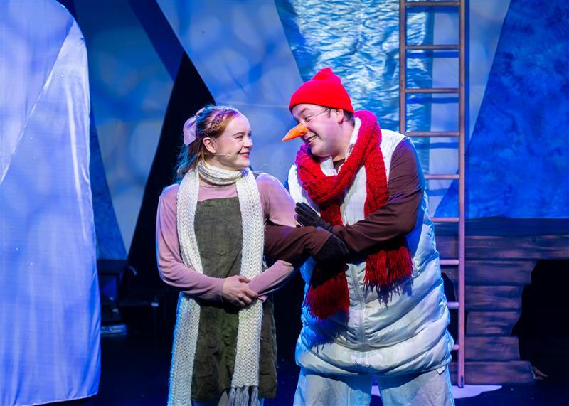 A man and woman dressed in vibrant costumes perform on stage, showcasing their talents in a lively theatrical setting.