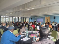 people sitting around tables and looking at a screen while a presenter is talking