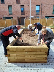 four people around a raised bed digging the soil so they can plant some plants