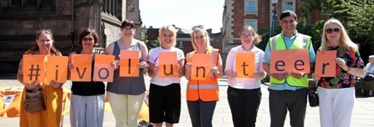 A row of smiling people holding up letters to spell #ivolunteer