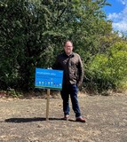 Cllr stands next to wildflower sign