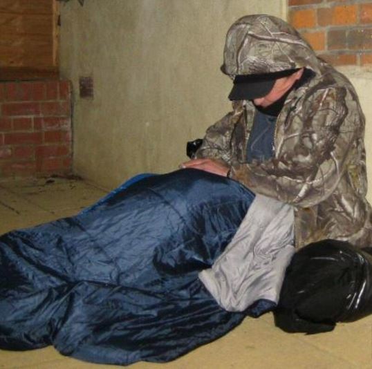 Man in large coat and sleeping bag, sat in doorway