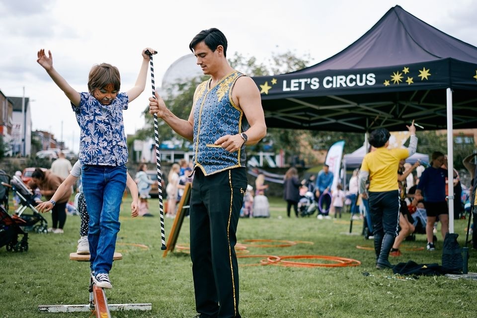 child on balance beam with circus artist at outdoor event