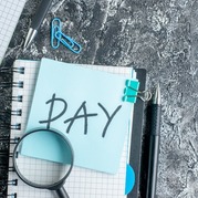 The word 'pay' on a blue post-it note with notebook and pen