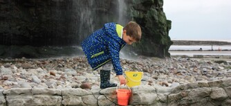 image of a child beachcombing and filling a bucket with his findings at St Audries Bay Somerset