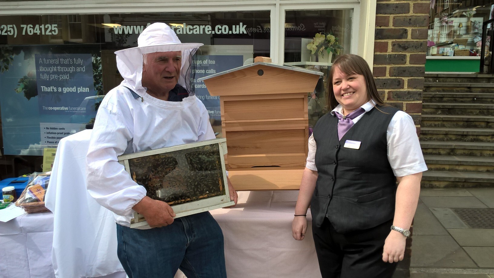 Southern Co-op Retail store staff member with a beekeeper in a protective suit holding a a box of bees