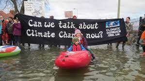 people in a dingy with a banner saying 'can we talk about climate change now?'