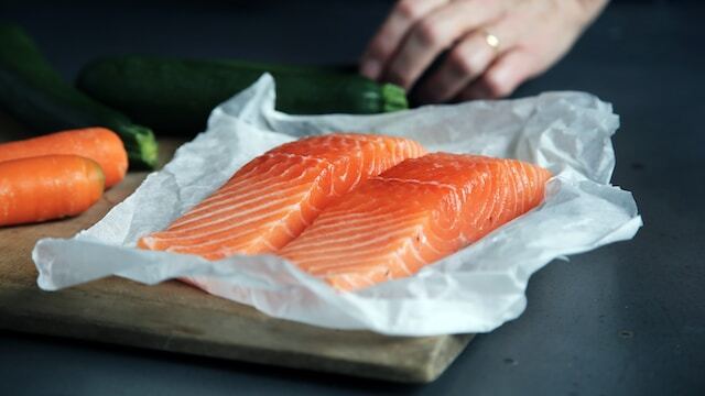 A couple of salmon fillets on greaseproof paper on a chopping board by CA Creative from Unsplash