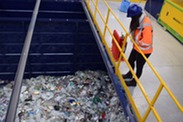 An employee in an orange hi-vis jacket and a blue hard hat stands on a balcony overlooking an area full of plastic