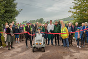 Group of people standing in front of red ribbon at the new path in Easton, while former HM Lord-Lieutenant of Somerset, Annie Maw cuts the ribbon