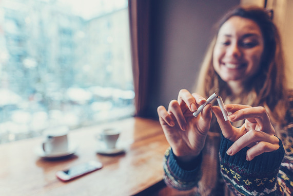 Young smiling woman sitting at the café and snapping her cigarette in half