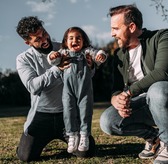 Male gay couple holding their little daughter in the air who laughs happily