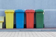 A yellow, blue, red and green wheelie bin on a pavement.