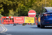 Traffic signs diverting a blue car around fenced-off road works.