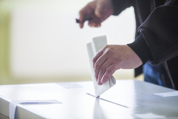 Hand dropping ballot paper into ballot box.