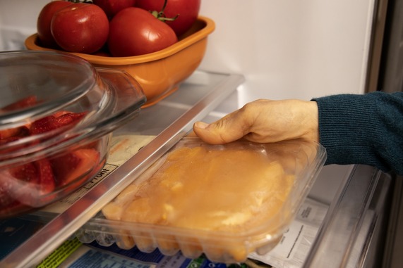 Hand placing a pack of chicken into a fridge.