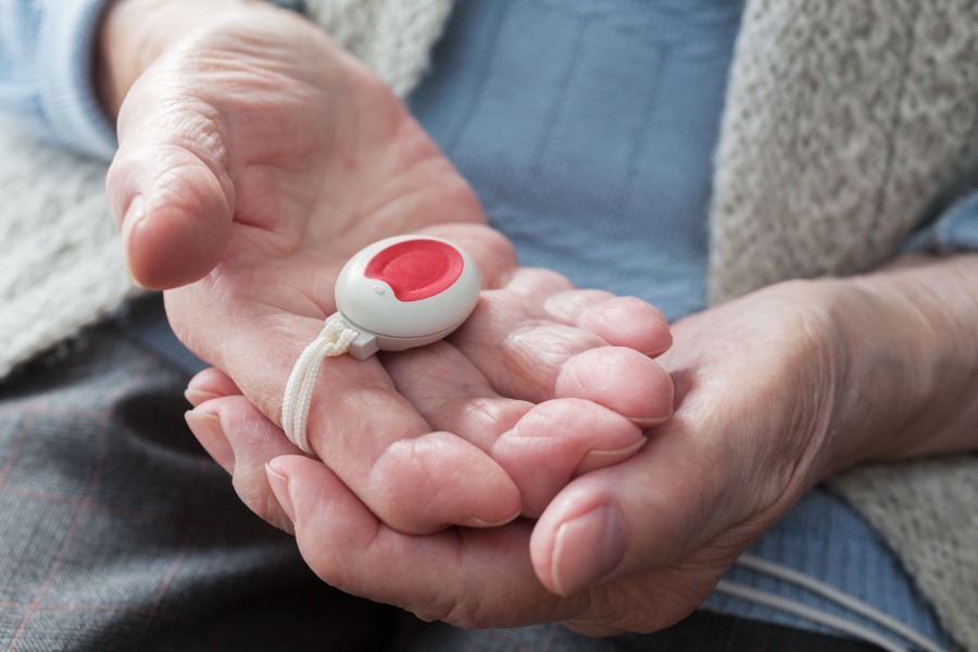 An elderly person holding a Lifeline alarm pendant.