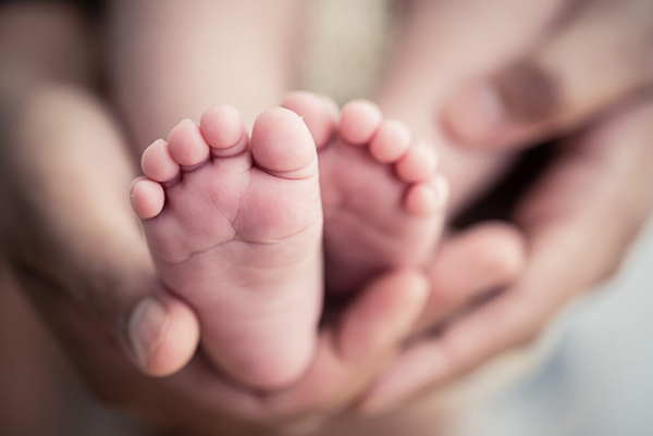 A pair of adult hands supporting the feet of a baby.