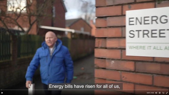 DESNZ's 'It all adds up' Twitter video thumbnail featuring TV presenter Dom Littlewood on Energy Street.