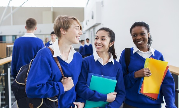 Secondary school children holding in blue uniforms, holding their bags and school files.