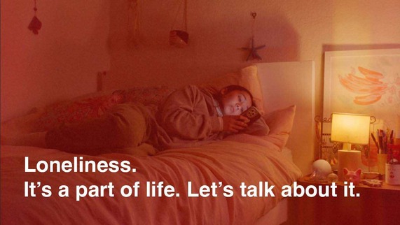 A lonely teenage girl looking at her mobile whilst lying on her bed, captioned: 'Loneliness. It’s a part of life. Let’s talk about it.'