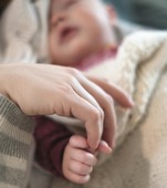 A mother's hand holding her baby's fingers.