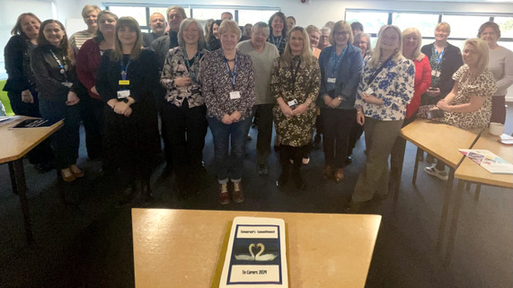 A group of people stand in front of a table which has a cake on it.