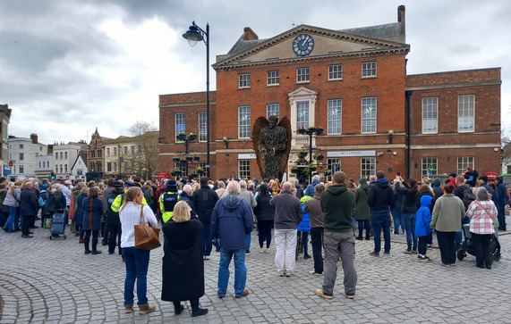 Large crowd of people looking up at the Knife Angel in front of Market House in Taunton.