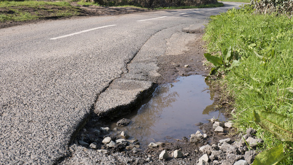 A large pothole on the side of a rural country road.