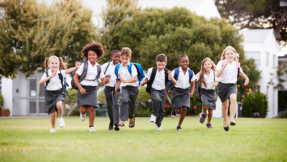 Multi-racial school children running accross a school playing field.