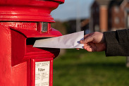 A hand posting an envelope through a red post box.