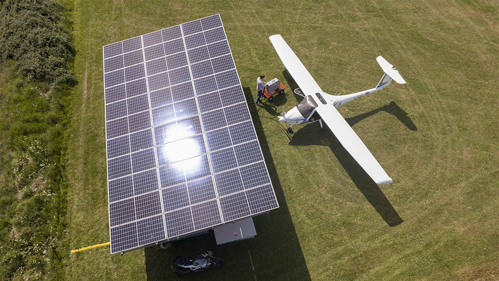 Aerial view of an electric powered 'Velis Electro', parked on a green field next to a solar panel array.