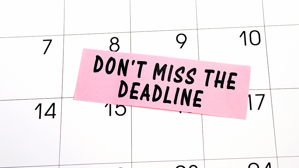 The phrase Don't miss the deadline written in black text on a pink sticky note posted to a calendar page as a reminder.