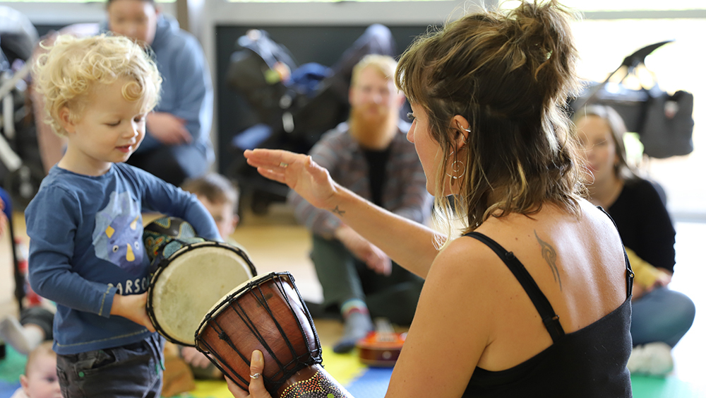 A female member of the Arts Engagement and Outreach team teaching a child how to play a bongo drum.