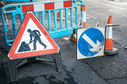 A barrier, traffic cone and road work signs placed on a freshly re-tarmacked road.