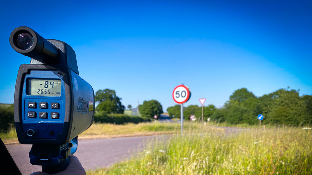 A handheld speed camera being used out the window of a car in a 50mph zone on a summer's day.