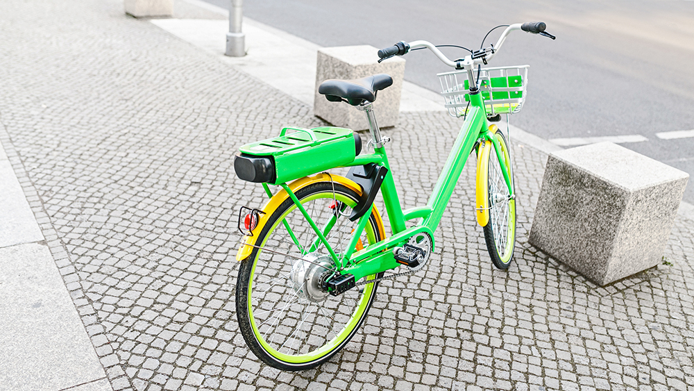 An lime green e-bike parked on a cobbled pavement with cube shaped stone bollards.