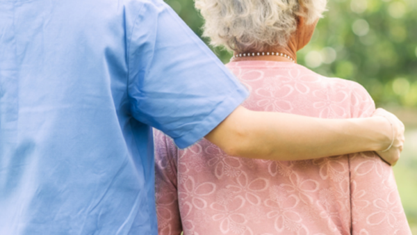 A carer with her arm around an elderly lady.