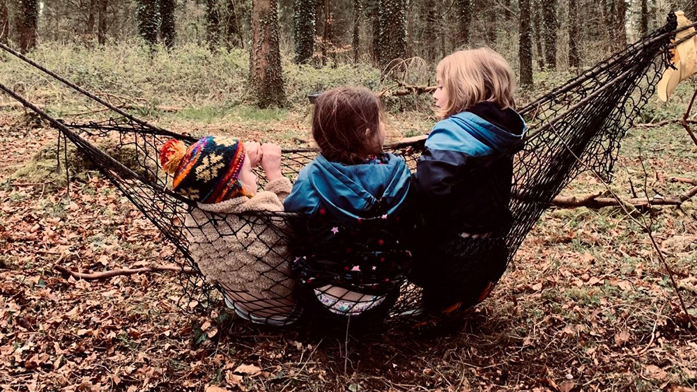 Three girls swinging in a hammock in a forest.