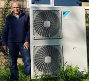 A man stood next to a air source heat pump fitted at his home, courtesy of Retrofit Somerset.