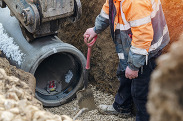 Stock image of groundworkers laying new concrete pipes during deep drainage work.