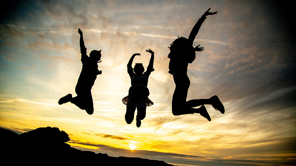 Three children having fun and jumping in the air against a sunset.