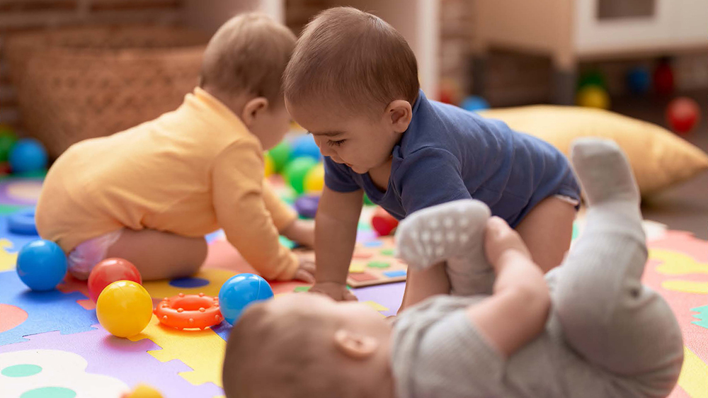 Three toddlers playing with toy balls on a play mat.