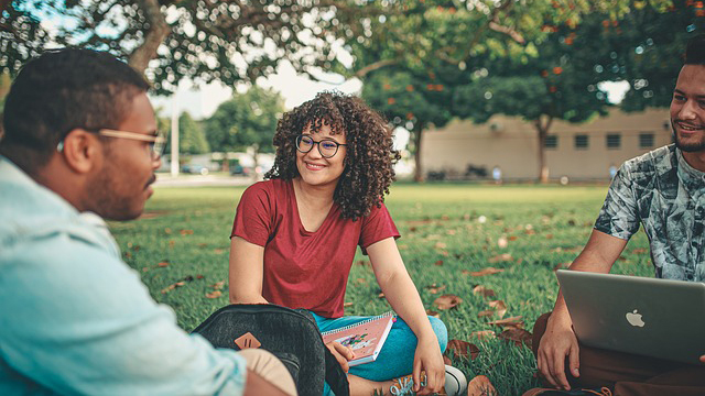 Stock image of three students studying whilst sitting on the grass.