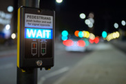 Pedestrian crossing button and illuminated wait sign with out of focus traffic in the background.