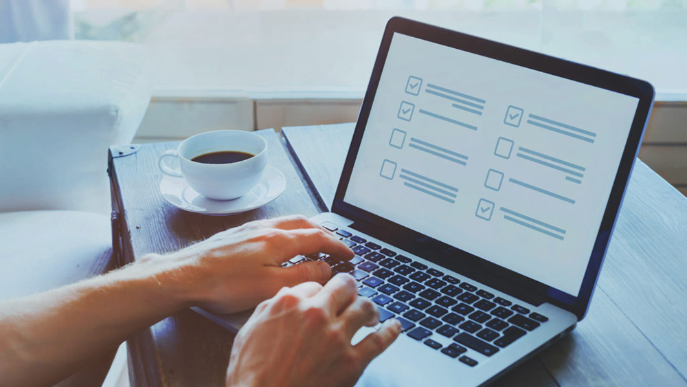 A person using a laptop to complete an on online with a cup of coffee in the background.