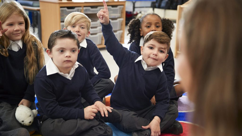 Special needs children in uniform sat cross-legged being taught at school.